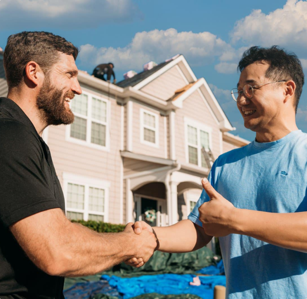 Two men shaking hands in front of house.