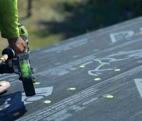 Worker using nail gun on roof underlayment.