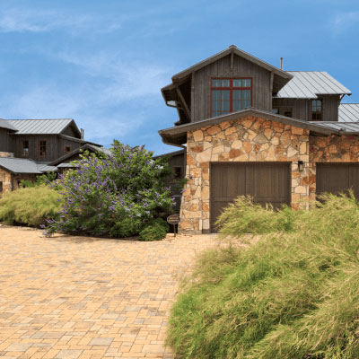 Rustic stone house with paved driveway and plants.