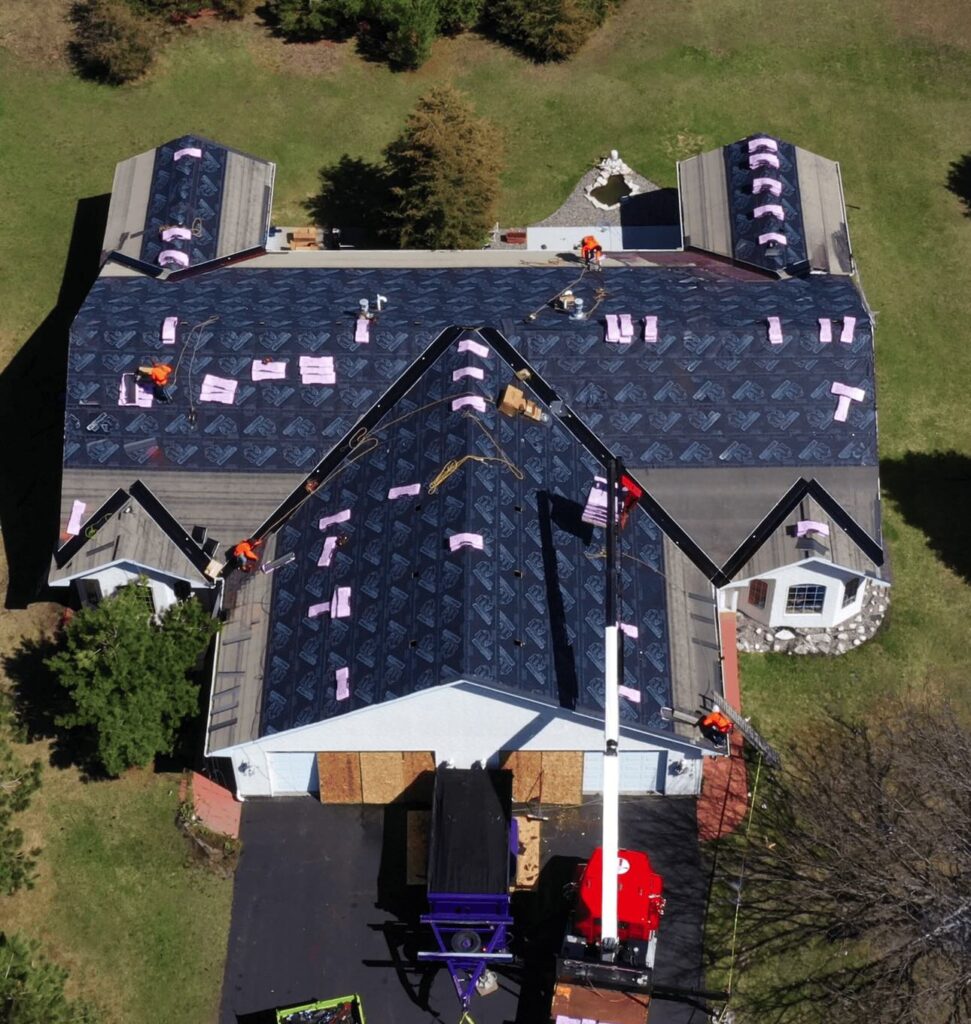 Workers installing new shingles on large house roof.